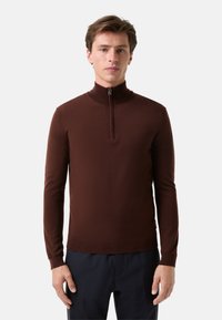 Brauner Zip-Kragen-Pullover aus weichem Strickmaterial. Figurbetontes Design mit langen Ärmeln und einem gerippten Saum, mit einem silbernen Reißverschlussdetail am Kragen.
