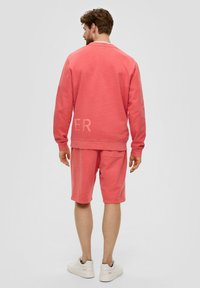 Sweat-shirt rose et shorts assortis, en mélange de coton, coupe décontractée. Les shorts ont une poche à l'arrière ; le sweat-shirt a des lettres texturées "ER" au dos.