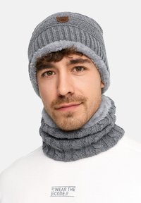 Bonnet en tricot gris avec une doublure en polaire grise douce et un col assorti. Présente une texture côtelée et une étiquette logo en cuir marron à l'avant.