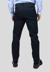 Pantalon noir à coupe droite, avec deux poches arrière et des détails de couture subtils, associé à des chaussures de ville noires.