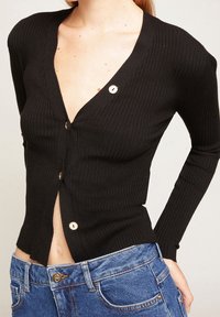 Czarny kardigan prążkowany z głębokim dekoltem w kształcie litery V, długimi rękawami i złotymi guzikami, w połączeniu z niebieskimi dżinsami.