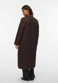 Cappotto lungo trapuntato marrone con colletto marrone, cuciture a contrasto e tasche laterali, caratterizzato da una vestibilità comoda e un orlo dritto.