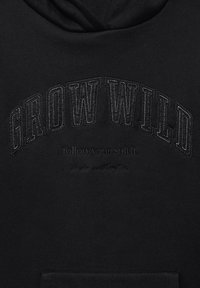 Felpa nera con cappuccio caratterizzata da un ricamo con la scritta "GROW WILD" e "follow your spirit" sotto, con una texture liscia e una tasca frontale.