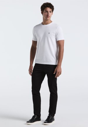 White cotton t-shirt with crew neckline and short sleeves, paired with fitted black pants and black sneakers. Small embroidered logo on shirt.