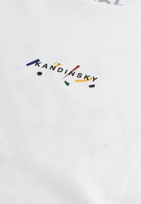 Balta medvilninė marškinė su juodu užrašu "KANDINSKY" ir spalvotais akcentais mėlynos, raudonos, geltonos, juodos ir žalios spalvų moderniame dizajne.
