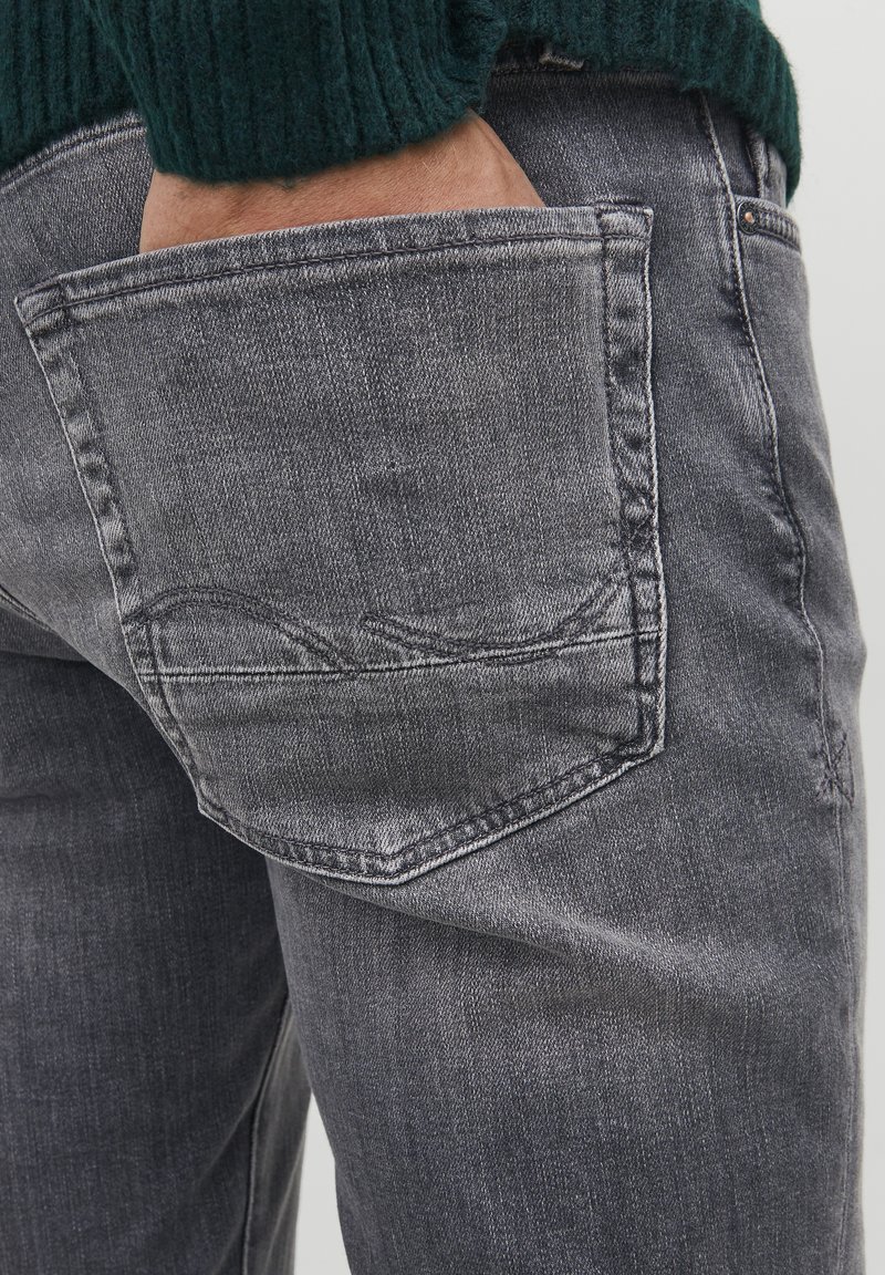 Jeans de mezclilla gris con un bolsillo trasero que presenta sutiles detalles de costura. La textura parece desgastada, con un corte de pierna recta.