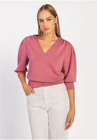 Roze V-hals top met pofmouwen, zachte stof en een aansluitende silhouet, gecombineerd met witte hoge taille broeken. Eenvoudige ontwerpdetails.