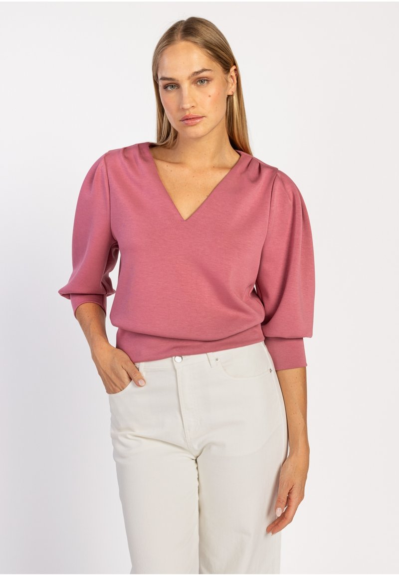 Roze V-hals top met pofmouwen, zachte stof en een aansluitende silhouet, gecombineerd met witte hoge taille broeken. Eenvoudige ontwerpdetails.