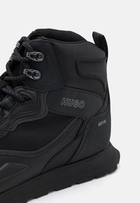 Zwarte high-top sneakers met een mix van textiel en synthetische materialen, voorzien van reflecterende accenten, logodetail en textuurpatronen.