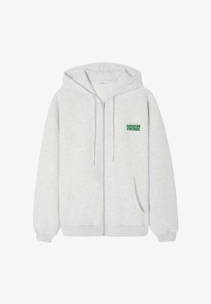 Harmaa vetoketjullinen huppari, joka on valmistettu pehmeästä kankaasta. Siinä on kengurun tasku ja vasemmassa rinnassa vihreä "AMERICAN VINTAGE" -logo.