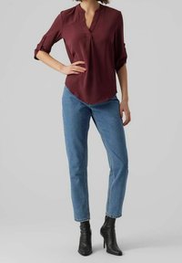 Blouse bordeaux avec un col en V et des manches retroussées, associée à un jean droit bleu clair. Le modèle porte des bottines à talons noires.