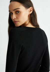 Maglione nero con scollatura rotonda e dettagli in cucitura intricata sulle cuciture delle spalle. Texture liscia, design aderente e maniche lunghe.