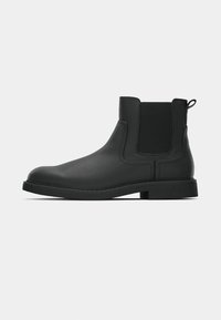 Botină din piele neagră, până la glezne, cu panouri laterale elastice, talpă din cauciuc texturat și un tab de prindere pe spate. Finisaj neted cu detalii de cusătură minime.