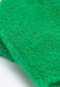 Tissu en fausse fourrure verte, texture douce, épaisse et duveteuse, avec une couleur vibrante. La surface présente de fines fibres créant de la profondeur et de la chaleur.