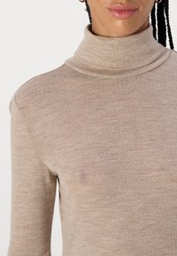 Beige høyhalset genser laget av et fint strikkemateriale med en tettsittende fasong og subtil tekstur. Ingen synlige mønstre eller metallisk utstyr.