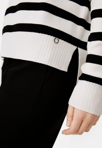 Maglione a righe bianco e nero, con polsini e orlo a costine, dotato di uno spacco laterale e un piccolo dettaglio ad anello in argento all'anca.