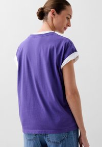 T-shirt en coton violet avec un col rond, des manches courtes dotées de revers blancs, et une coupe décontractée. Design simple sans motifs.