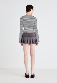 Pruhovaný top s dlouhým rukávem v černé a bílé barvě, spárovaný s úzkou šedou flared minisukní. Modelka má na sobě robustní černé boty.