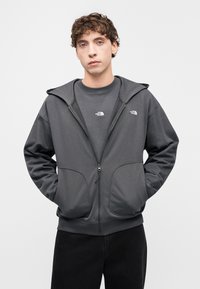 Γκρι φούτερ με φερμουάρ κατασκευασμένο από λεία ύφασμα, με δύο μπροστινές τσέπες, διπλό λογότυπο στο στήθος και άνετη κουκούλα.