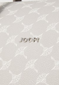 Matériau texturé gris clair avec un motif en relief et un logo métallique "JOOP!". Le design intègre des motifs complexes à travers l'ensemble.