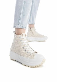 Zapatillas altas en color crema claro con un patrón texturizado, suela blanca y cordones. Cuentan con una cremallera lateral y una puntera de goma.