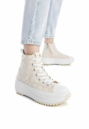 Zapatillas altas en color crema claro con un patrón texturizado, suela blanca y cordones. Cuentan con una cremallera lateral y una puntera de goma.