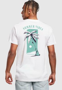 Hvit T-skjorte med et palmetre-grafikk i teal og svart med teksten "SUMMER VIBES" over, kortermet og med en avslappet passform.