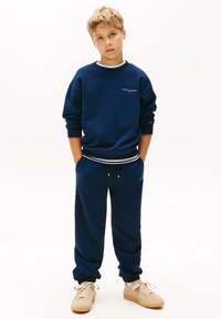 Marineblauwe sweatshirt en bijpassende joggers van zachte stof, met witte accenten en trekkoorddetails. Effen textuur, relaxed fit.