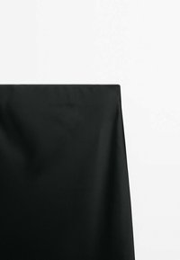 Sort stof draperet over en overflade, med en glat tekstur og subtile folder. Baggrunden er ensfarvet hvid, hvilket fremhæver stoffets farve.