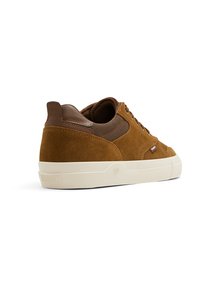 Baskets en daim marron avec panneaux en maille, semelle en caoutchouc clair et branding subtil sur le côté et à l'arrière. Les lacets sont marron.