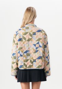 Giacca trapuntata con un design a patchwork nei colori pastello e motivi geometrici, maniche lunghe e colletto rotondo. Gonna pieghettata nera.