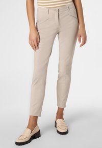 Béžové kalhoty na míru s slim fit střihem, s bočními kapsami a hladkým povrchem. V kombinaci s krémovými mokasíny a pruhovaným topem.
