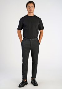 Must t-särk lühikeste varrukatega, kombineeritud tumeda halli kohandatud pükstega ja mustade kingadega. Lihtne disain, sile tekstuur ja klassikaline istuvus.