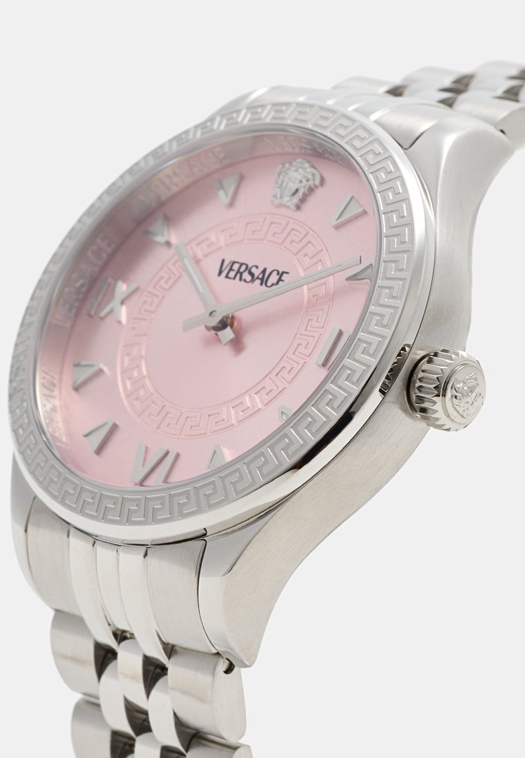 Montre en acier inoxydable avec un cadran rose, motif en relief de clé grecque sur la lunette, index horaires argentés et une couronne avec un accent de logo.