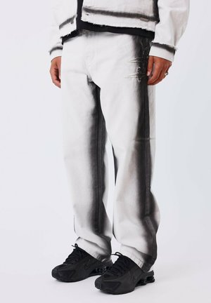 Witte denim broek met een gradient zwart ontwerp, versleten details, een losse pasvorm en gecombineerd met zwarte sneakers.