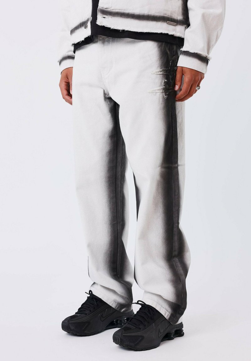 Pantalones de mezclilla blancos con un diseño degradado en negro, detalles desgatados, corte holgado y combinados con zapatillas negras.