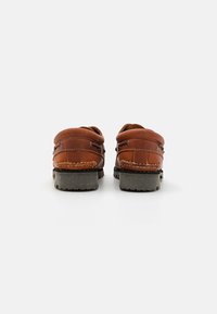 Pair of brown leather moccasin shoes with thick black rubber soles, viewed from the back against a white background.