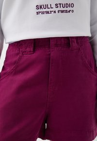 Korte broek in donkerpaars denim, met een klassieke snit, zijzakken, een rits aan de voorkant en riemlussen. De stof heeft een soepele textuur.