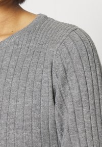 Harmaa neulepusero, jossa on V-aukko ja resorineulos; lähikuva olkapäästä, jossa näkyy hienoja pystysuoria viivoja ja pehmeä kangas.