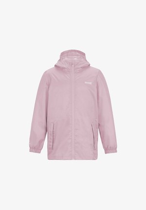 Jong meisje draagt een blauw gestreepte bucket hat, een roze jas over een roze fleece, zwarte cargoshorts, witte sokken en beige sneakers, glimlachend.