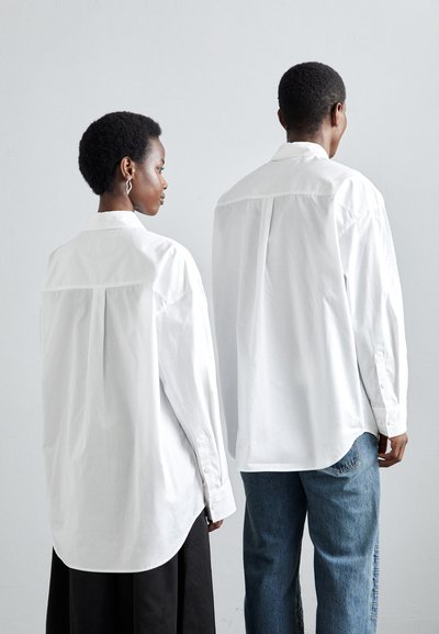 Hvite oversized skjorter med lange ermer, med avrundet kant og bakfold. Brukes med blå jeans og et svart skjørt.