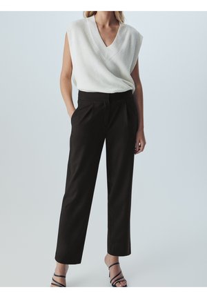 Top en tricot sans manches blanc avec un col en V, associé à un pantalon noir taille haute ajusté. Le modèle porte des sandales noires à lanières.