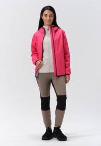 Rosa vattentät jacka med huva, vit inre lager, beige och svarta smalnande byxor, samt svarta sneakers. Slät textur genomgående.