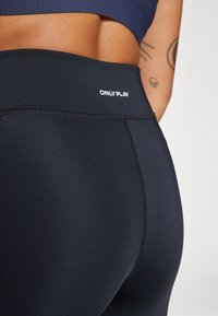 Κοντινό πλάνο ενός ατόμου που φοράει μαύρο ψηλόμεσο κολάν με την επωνυμία "ONLY PLAY" στη μέση και με ορατό τατουάζ στο μπράτσο του.