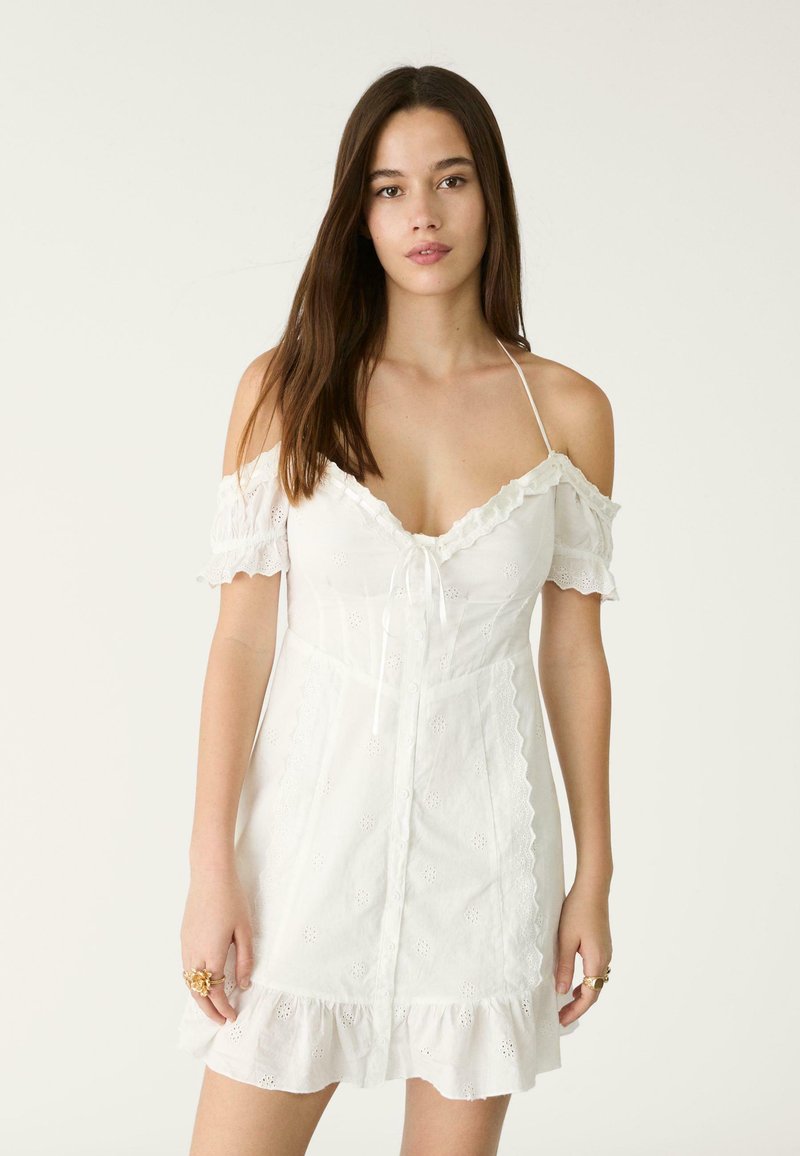 Witte off-shoulder jurk gemaakt van lichtgewicht stof, met ruffles aan de mouwen, decoratieve oogjes patronen en een knoopsluiting aan de voorkant met een gegolfde zoom.