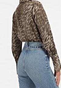 Blusa leopardata marrone e beige con maniche lunghe, vestibilità tailored e colletto, abbinata a jeans in denim blu a vita alta.