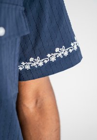 Mørkeblå skjorteærme med subtile teksturerede striber, der har hvid blomsterbroderi langs kanten.