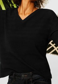 Czarny sweter z dekoltem w serek o teksturowanym wzorze, z długimi rękawami i luźnym krojem. W połączeniu z ciemnoniebieskimi dżinsami.