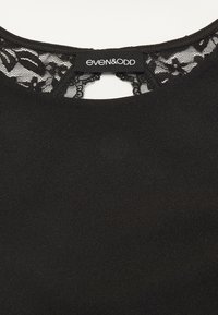 Schwarze Bluse mit Spitze am Ausschnitt. Sie hat eine runde Form, eine glatte Textur und einen Ausschnitt in Schlüsselloch-Optik. Das Etikett trägt die Aufschrift "even&ODD".