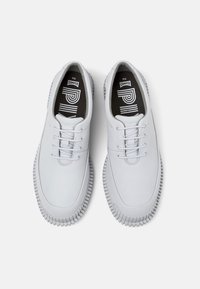 Chaussures en cuir blanc avec bout rond, design à lacets et semelle extérieure en caoutchouc texturé. Les semelles intérieures noires présentent un logo blanc et des motifs linéaires.